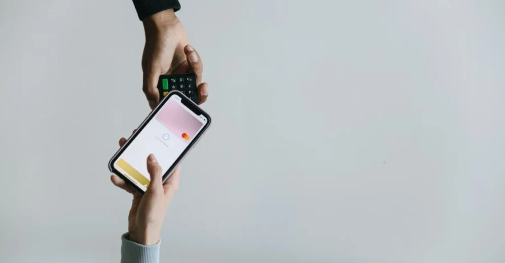 Hand holding smartphone displaying payment app interface above contactless card reader for influencer payment platforms.