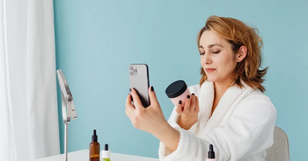 Woman reviewing affiliate tracking software on smartphone while displaying cosmetic product against blue background.