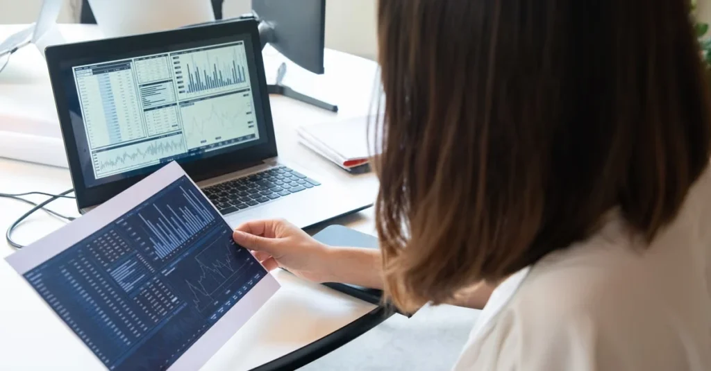 Woman reviewing affiliate program software analytics dashboard on laptop and tablet at desk.